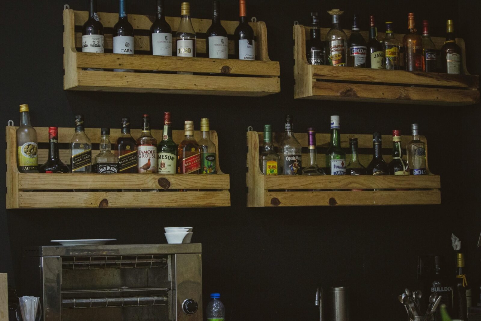 A rustic wooden shelf display of liquor bottles on a dark wall, perfect for a bar setting.